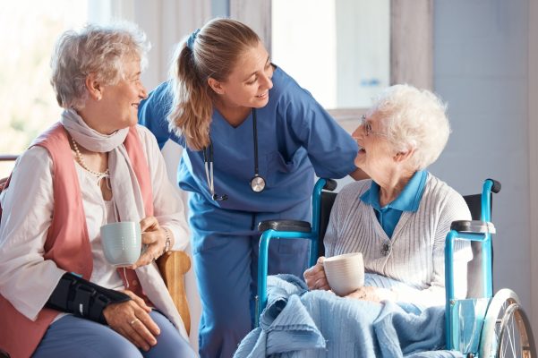 Nursing home, care and nurse with senior women doing healthcare checkup, examination or consultation. Medical, conversation and elderly woman in wheelchair consulting a doctor at retirement facility.